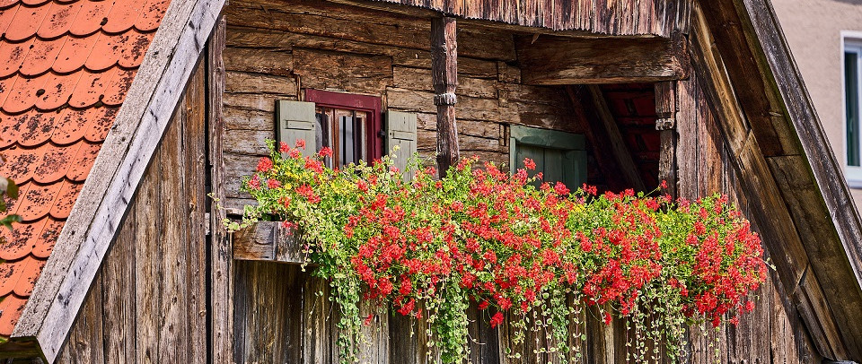 Holzhaus mit Balkon an dem Blumenkästen mit roten Blumen hängen