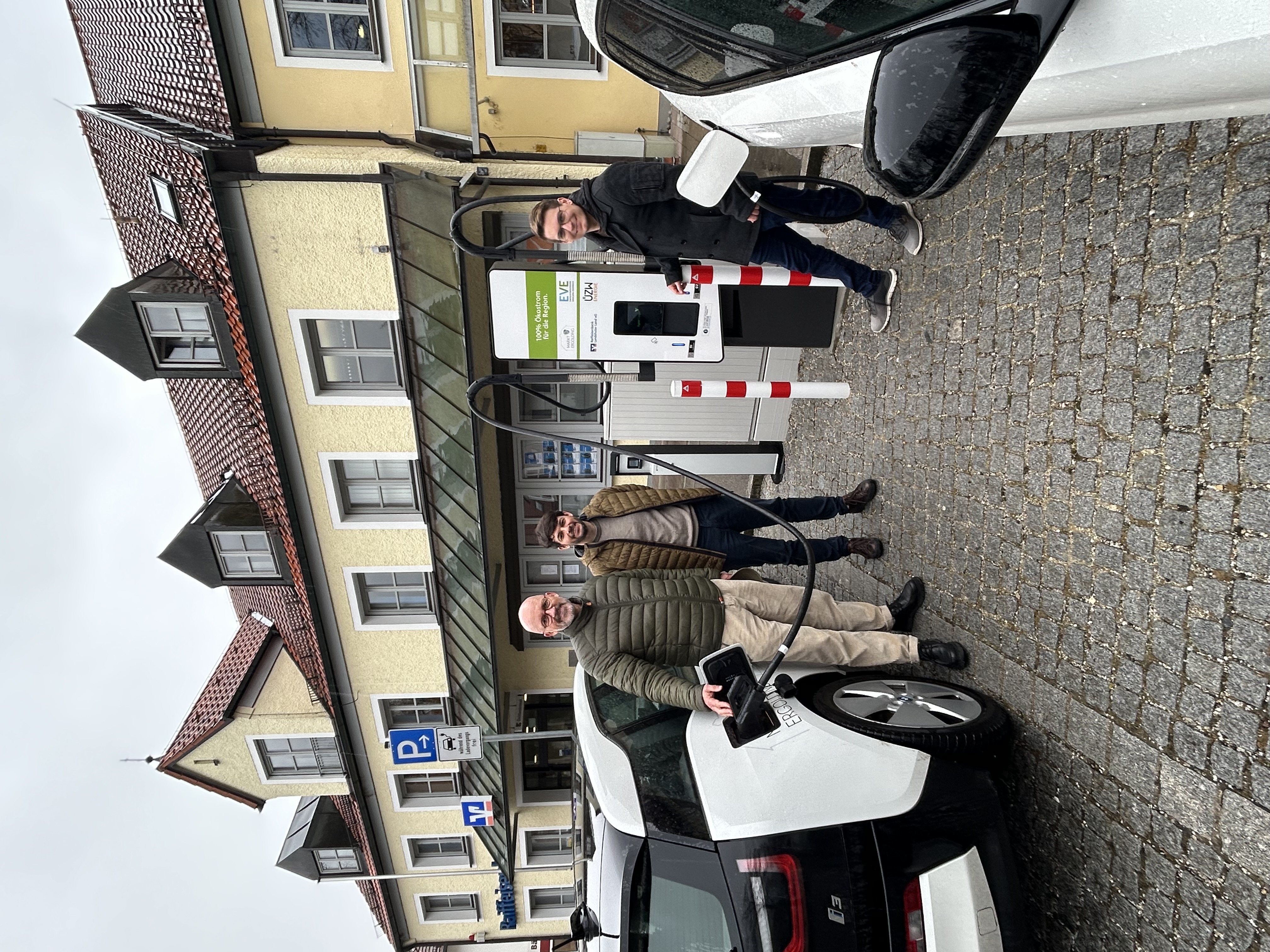 Drei Männer stehen bei der Inbetriebnahme einer Ladesäule zwischen zwei Elektroautos, die gerade laden.